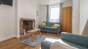A living room with a fireplace, a sofa, a TV, and a wooden door. - 2 South Street (Wigton)