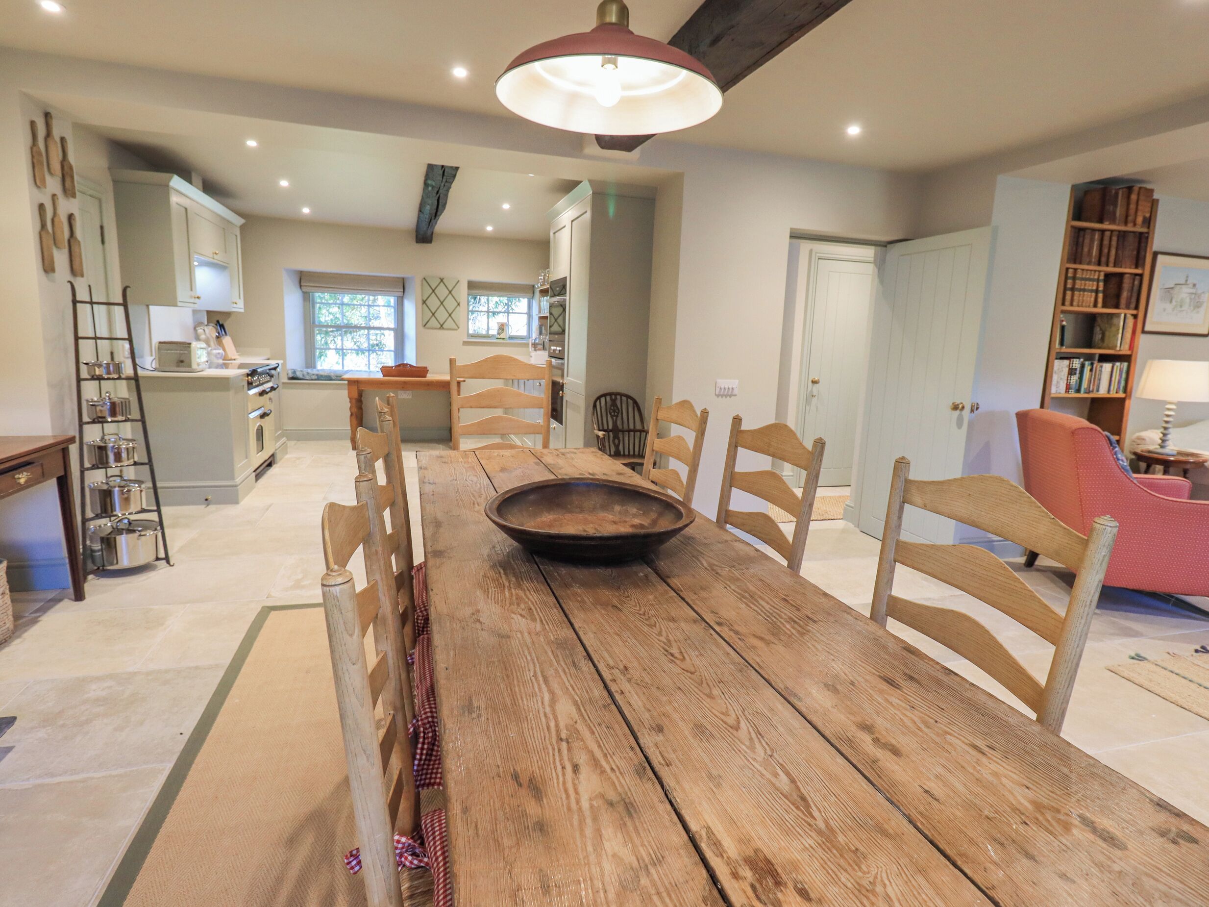 A spacious dining area with a wooden table and chairs, a kitchen in the background, and a bookshelf.