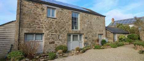 A stone house with a gravel driveway, a small garden, and a solar panel on the roof.