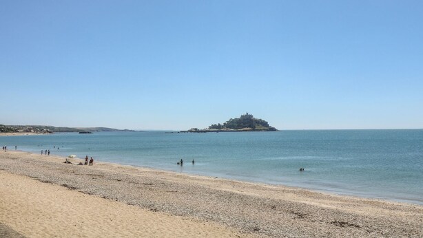 A beach with a pebbly shore and a distant island with ruins.