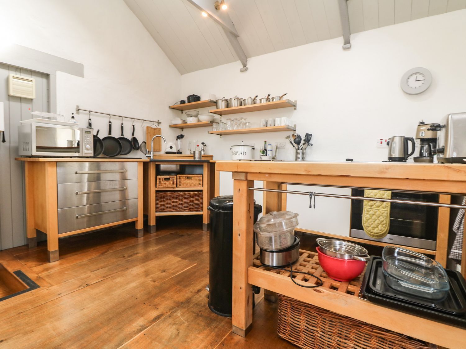 A compact kitchen with wooden cabinets, a microwave, and various utensils on shelves.