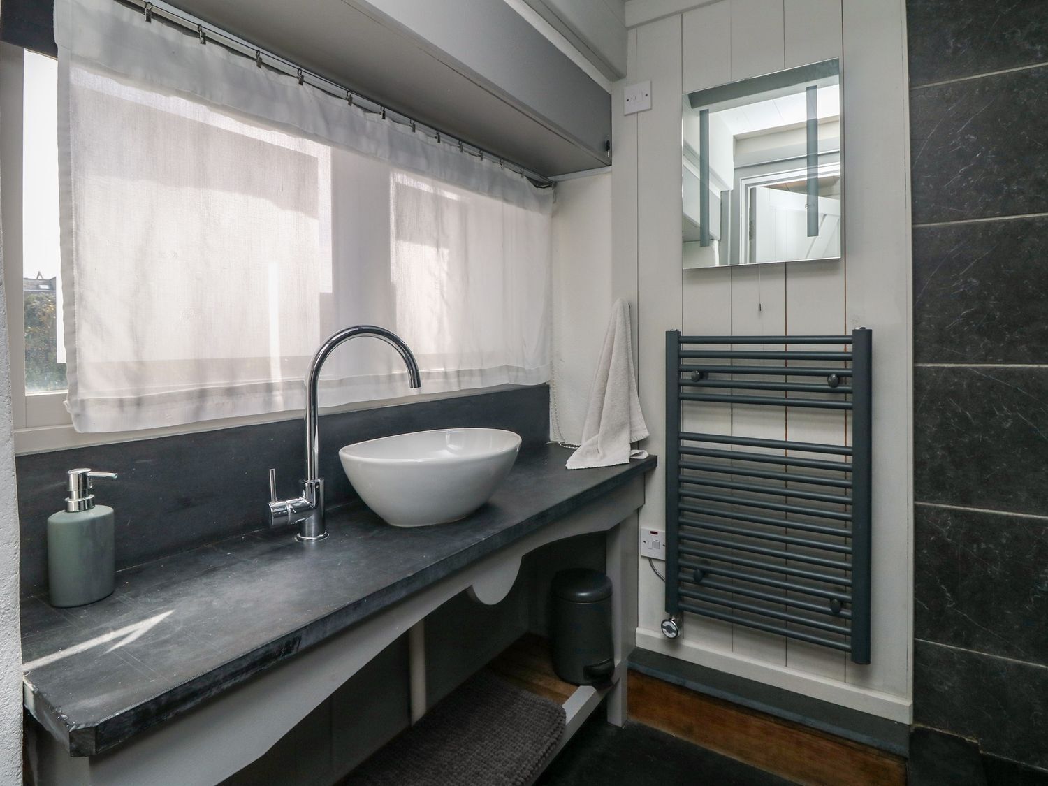 Un baño moderno con un lavamanos blanco, un perchero y un ventanal con cortinas de gasa.
