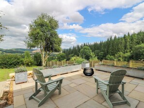 An outdoor patio with two Adirondack chairs, a fire pit, and a view of a forested landscape. - Oak Apple Cottage (Presteigne)