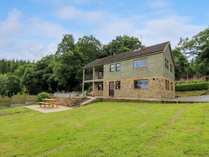 A two-story stone house with a balcony, a stone patio, and a grassy yard. - Oak Apple Cottage (Presteigne)