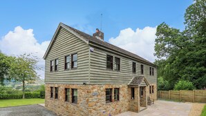 A two-story stone cottage with a stone foundation and wooden siding, a paved driveway, and a view of the surrounding landscape. - Oak Apple Cottage (Presteigne)