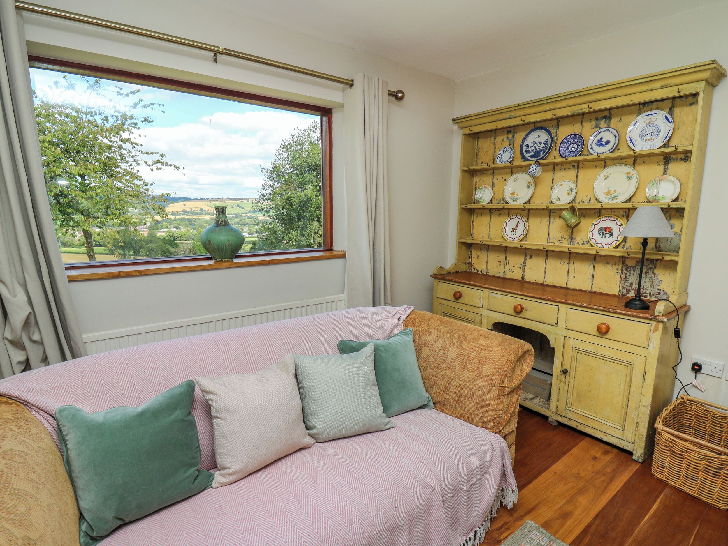 A bedroom with a bed, a dresser with a lamp, and a window with a view of greenery.