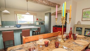A dining area with a wooden table set for four, surrounded by chairs, and a kitchen in the background. - Oak Apple Cottage (Presteigne)