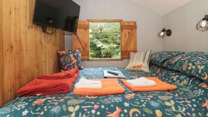 Una habitación acogedora con cama, televisión y ventana con vistas a árboles.