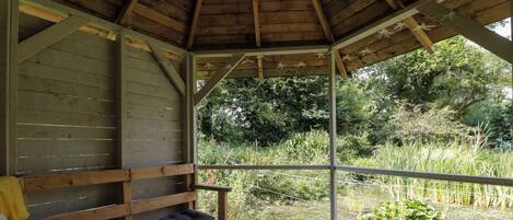 A wooden deck with a bench and a small table, overlooking a pond with lily pads.