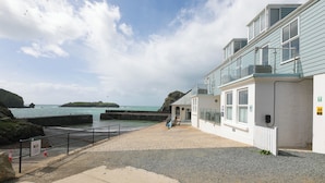 Un edificio costero con balcón que da al mar, un camino empedrado y una costa rocosa.