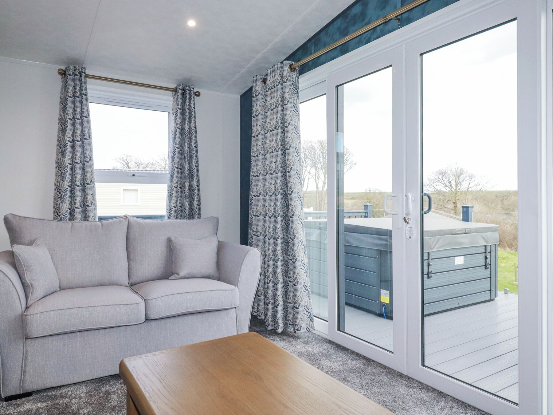 Una habitación con un sofá gris, una mesa de madera y un ventanal corredero que da a una terraza exterior.