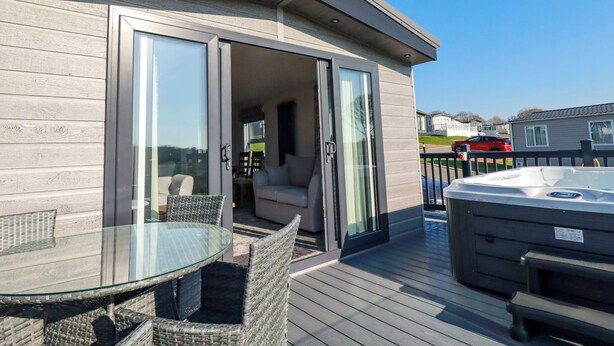 Una terraza con mesa de vidrio, sillas de mimbre, un jacuzzi y un ventanal corredera que da a un espacio interior.