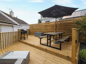 Une terrasse en bois équipée d’un barbecue, d’une table de pique-nique et d’un parasol.
