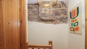 Una escalera de madera con un muro de piedra y una lámpara colgante.
