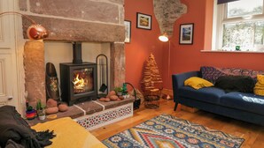Una sala de estar acogedora con chimenea de piedra, un sofá azul y un tapete estampado.