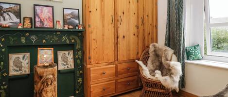 Una habitación acogedora con un armario de madera, una silla de mimbre y una chimenea decorada con arte en la pared.