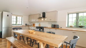 Une cuisine moderne avec une table en bois, des chaises, un four encastré et une fenêtre donnant sur un paysage verdoyant.
