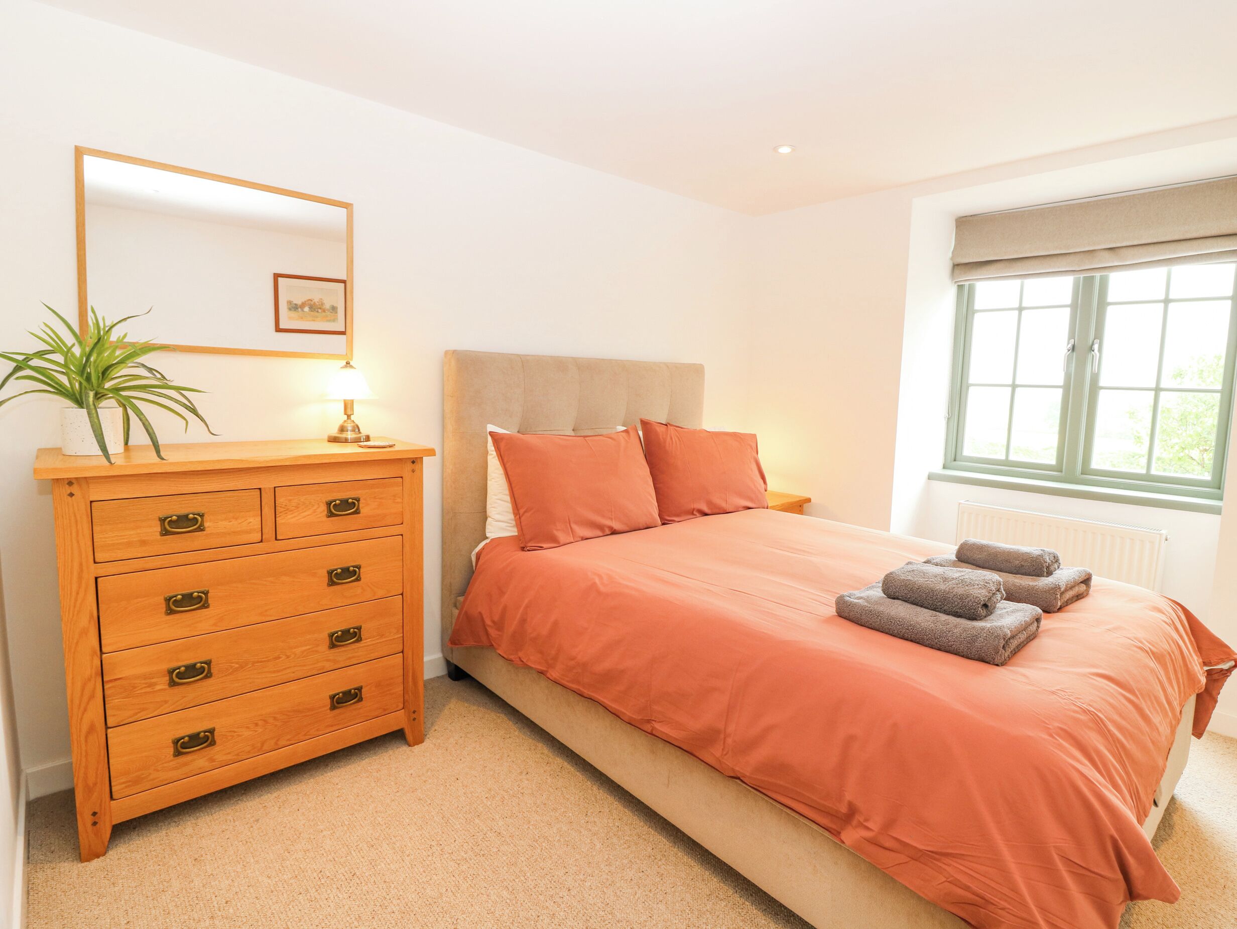Une chambre à coucher avec un lit, une commode, une lampe, une plante et une fenêtre.