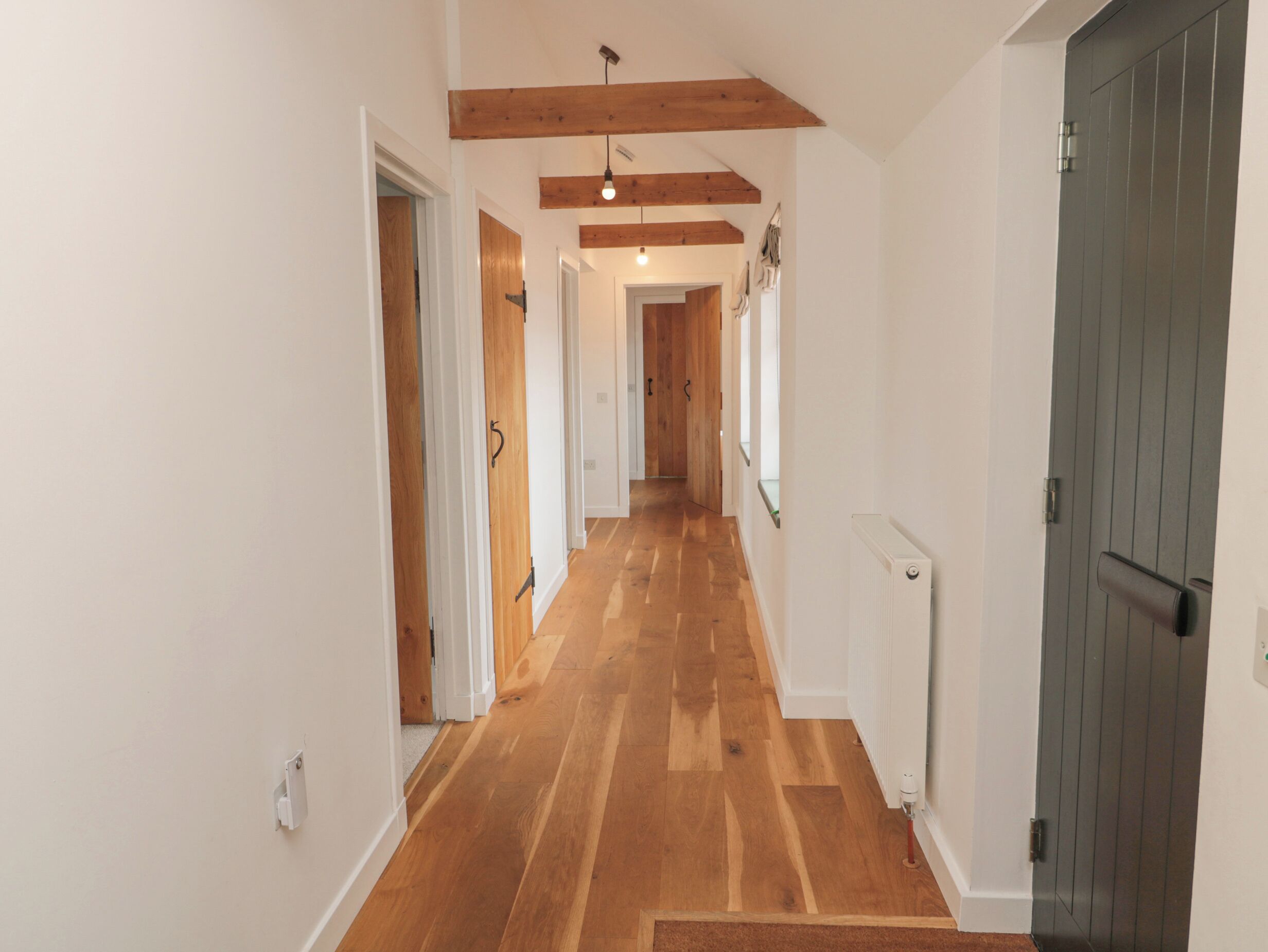 A hallway with wooden floors and white walls, leading to a dark wooden door.