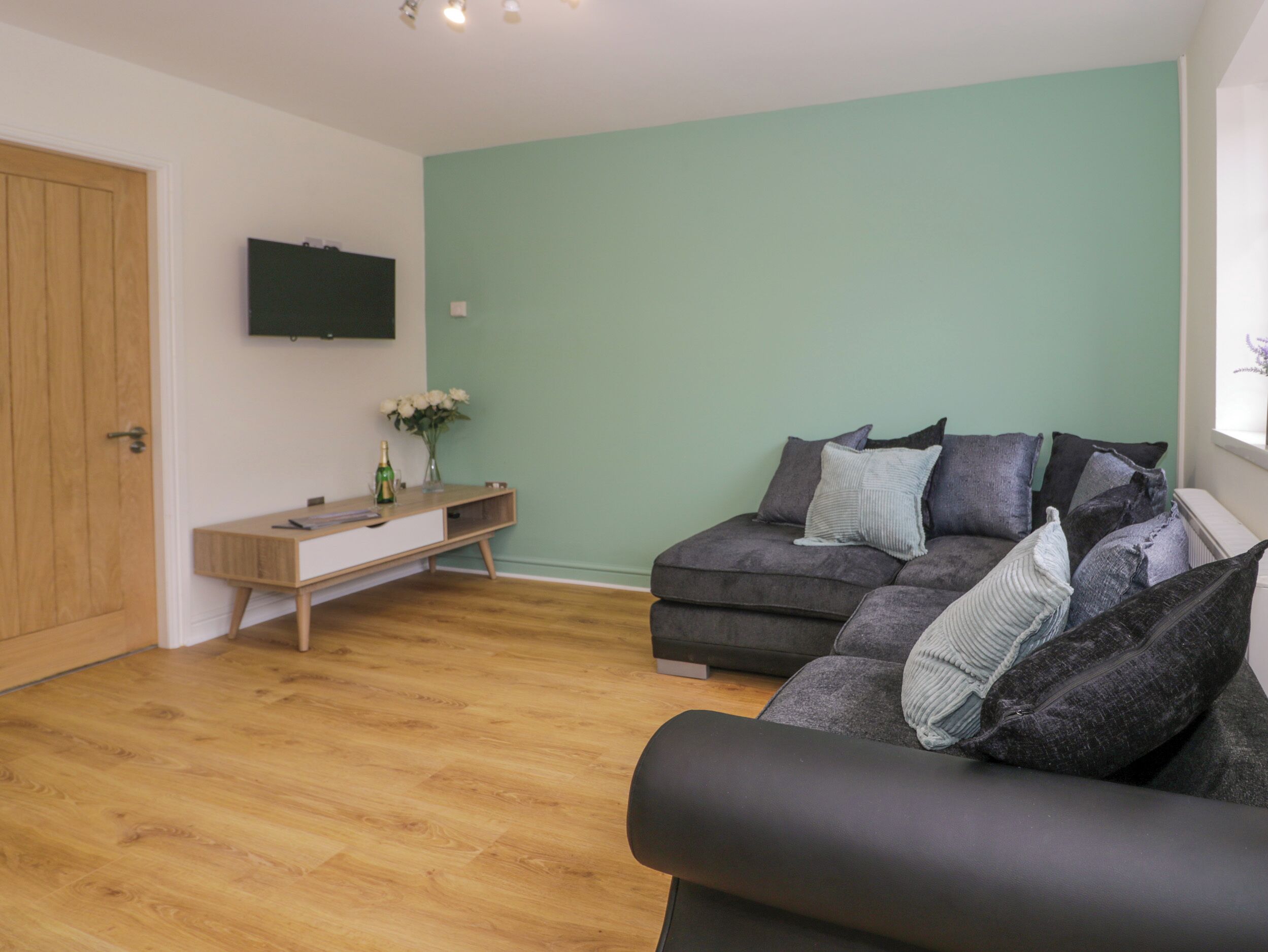 A living room with a grey sofa, a wooden coffee table, and a flat-screen TV mounted on the wall.