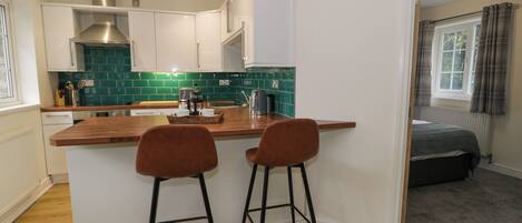 A compact kitchen with a wooden island, two bar stools, and a view into a bedroom.