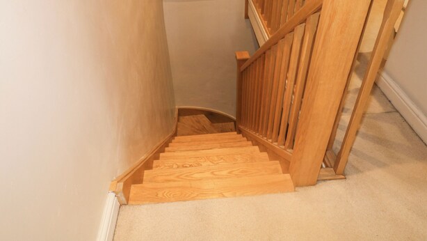 Un escalier en bois avec une rampe, des marches recouvertes de moquette et un mur blanc.