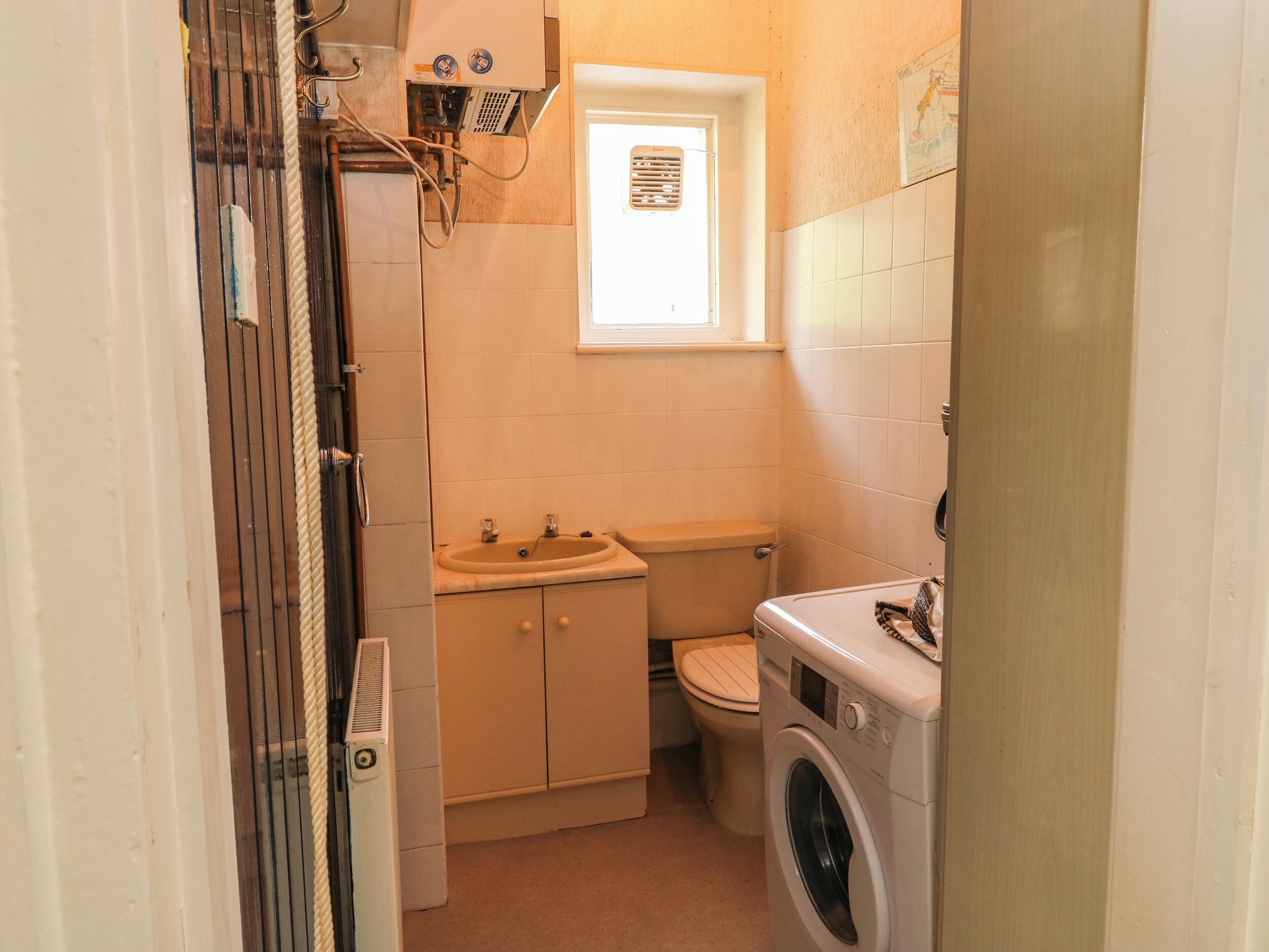 Et lille badeværelse med toilet, håndvask og vaskemaskine.