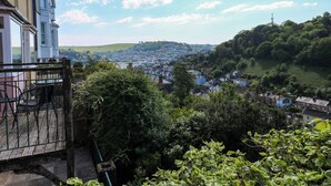 Un balcon donnant sur une ville, avec de la verdure et une colline visible au loin.
