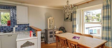 A kitchen with wooden cabinets, a dining table with chairs, a chandelier, and a view of the outside through a window.