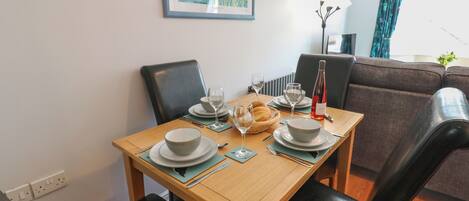 A dining table set with plates, bowls, glasses, and a bottle, surrounded by black chairs.