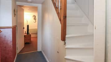 Un pasillo estrecho con una escalera de madera a la derecha, que lleva a una habitación con una puerta al final.