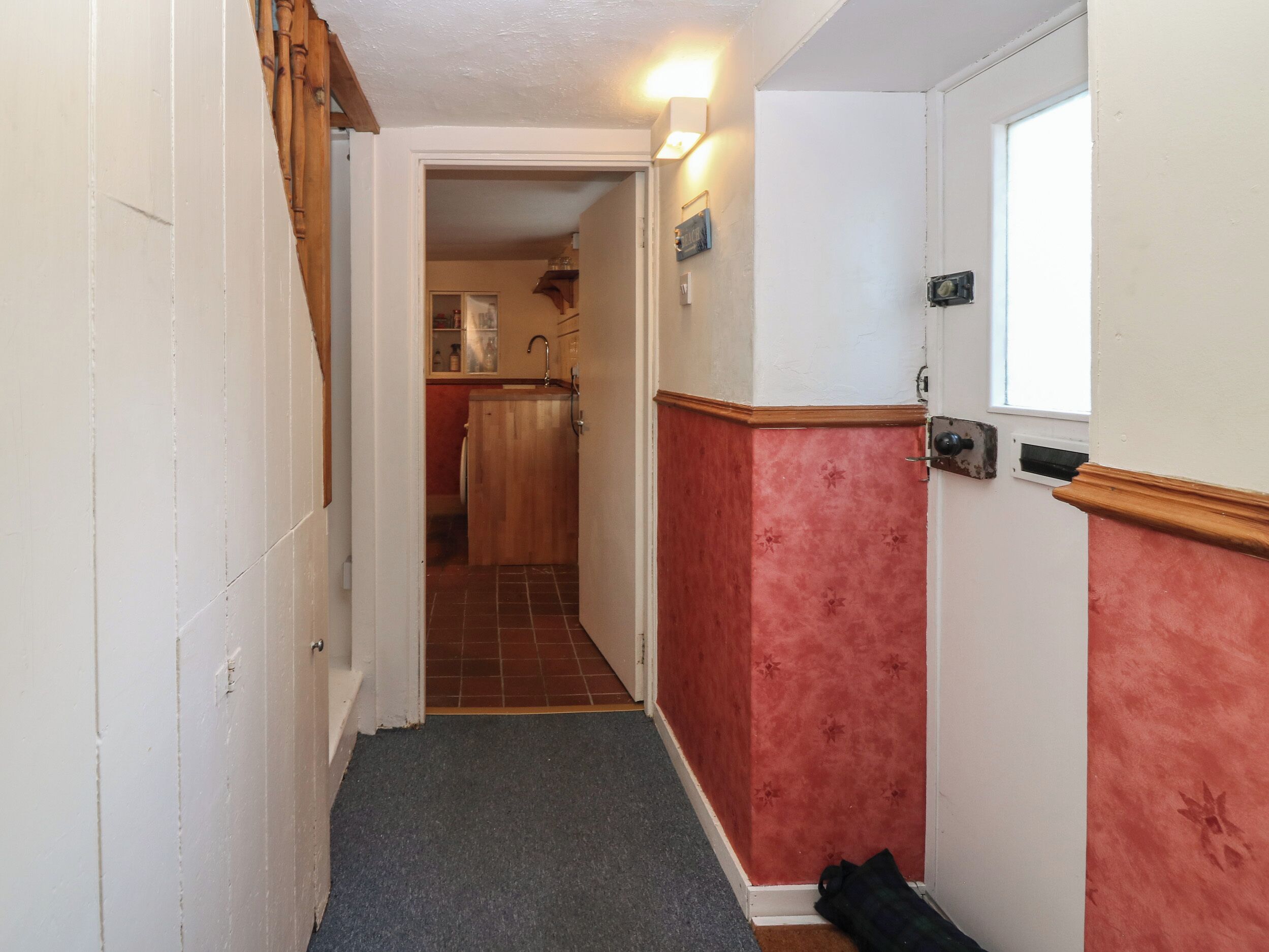 A narrow hallway with a wooden door on the left, a red wall on the right, and a small window at the end.