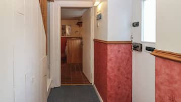 A narrow hallway with a wooden door on the left, a red wall on the right, and a small window at the end.