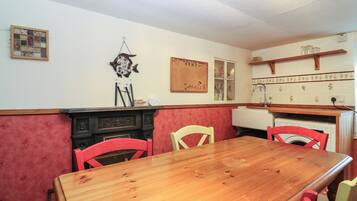Un comedor con una mesa de madera y sillas rojas, un banco acolchado de color rojo, un reloj de pared y un tablón de corcho con dibujos.