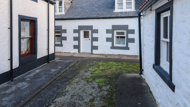 Ein schmaler Gang mit einem weißen Gebäude, das ein geometrisches Muster an der Wand, eine Tür und ein Fenster mit rotem Rahmen aufweist.