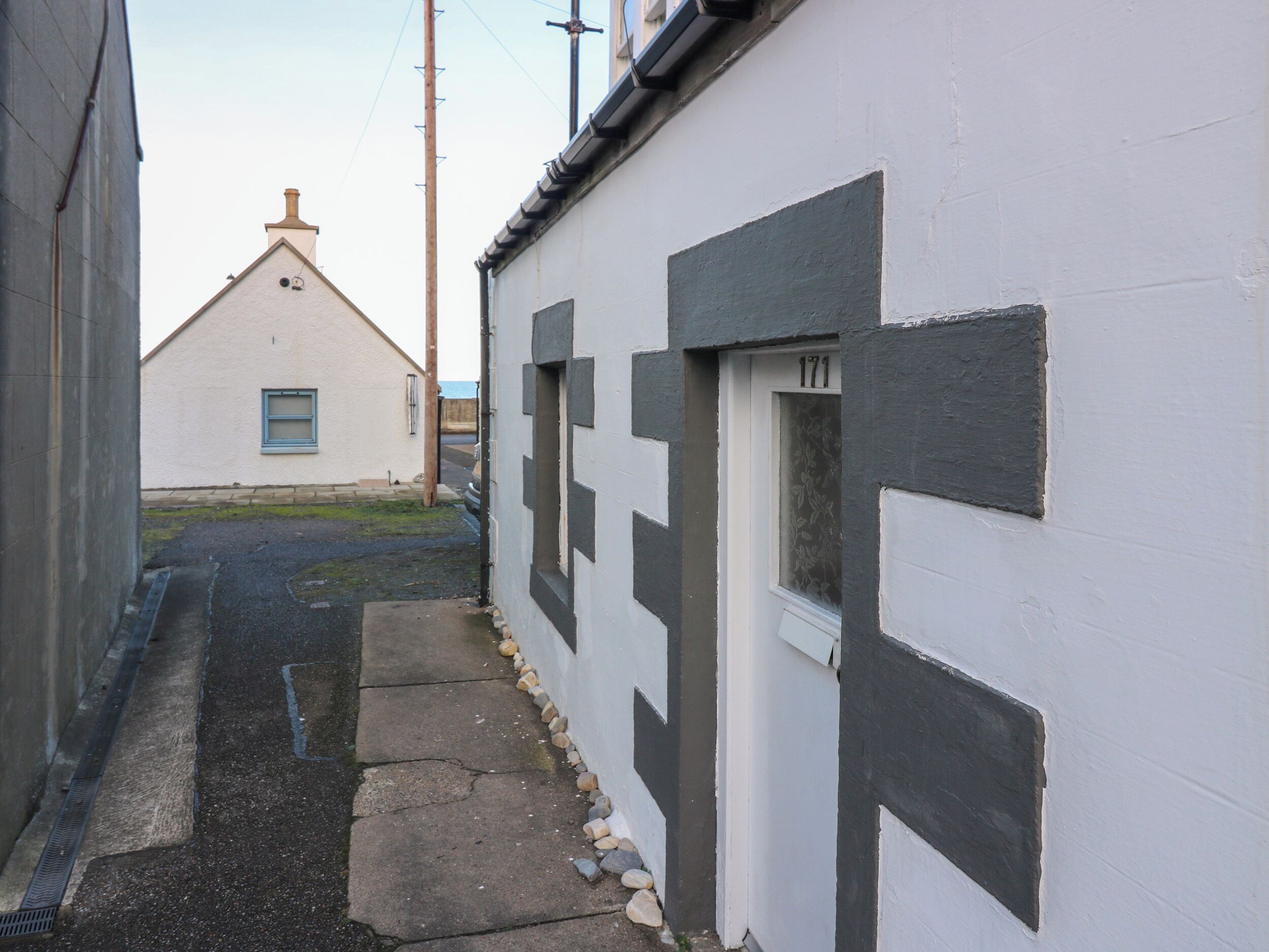A narrow alleyway with a white building on the right, a window with the number 171, and a small window on the left.