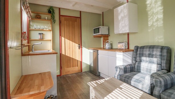 A compact living space with a kitchenette, a dining area, and a seating area. - Nŷth Y Bioden (Caernarfon)