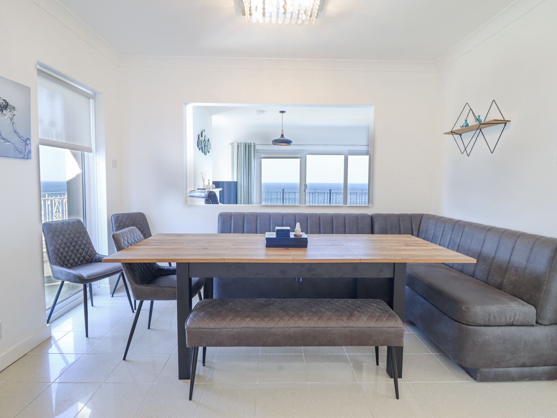 Un espace de restauration moderne avec une table en bois, des sièges confortables et une vue sur la mer grâce à de grandes fenêtres.