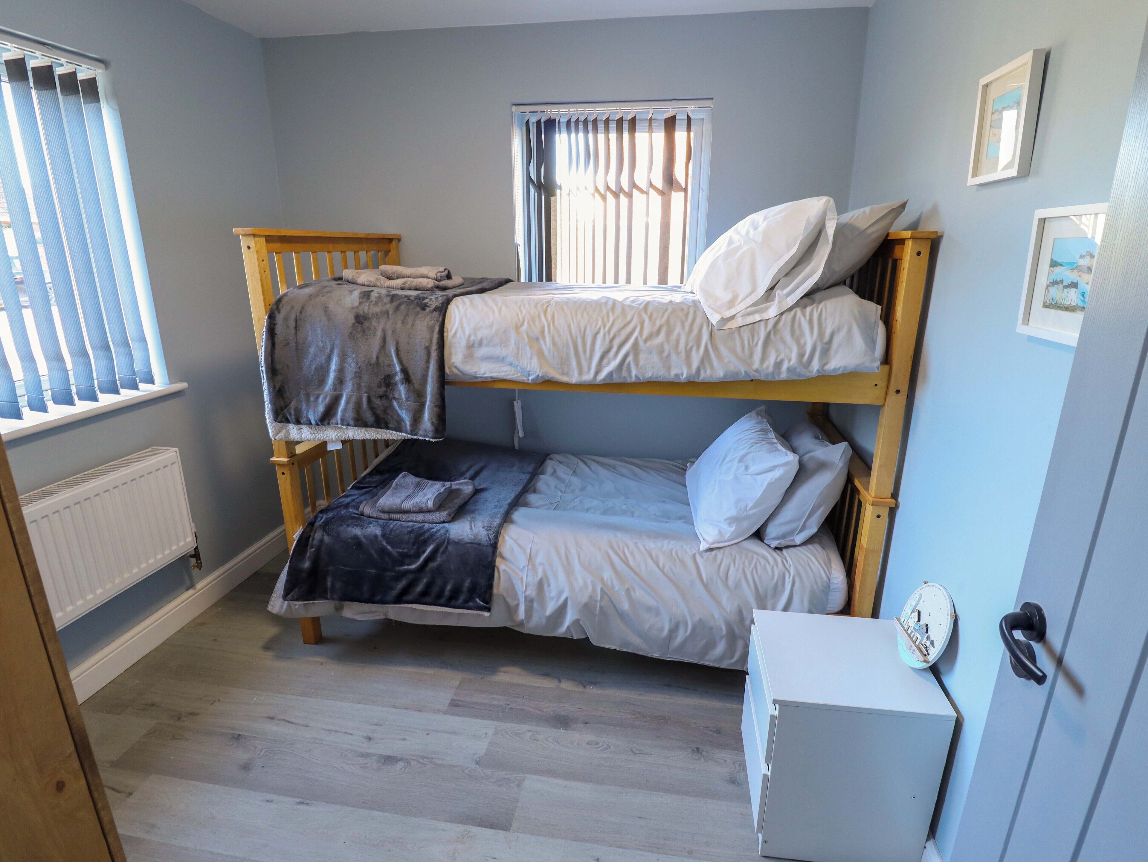 A bunk bed room with a white radiator, a small white cabinet, and a window with blinds.