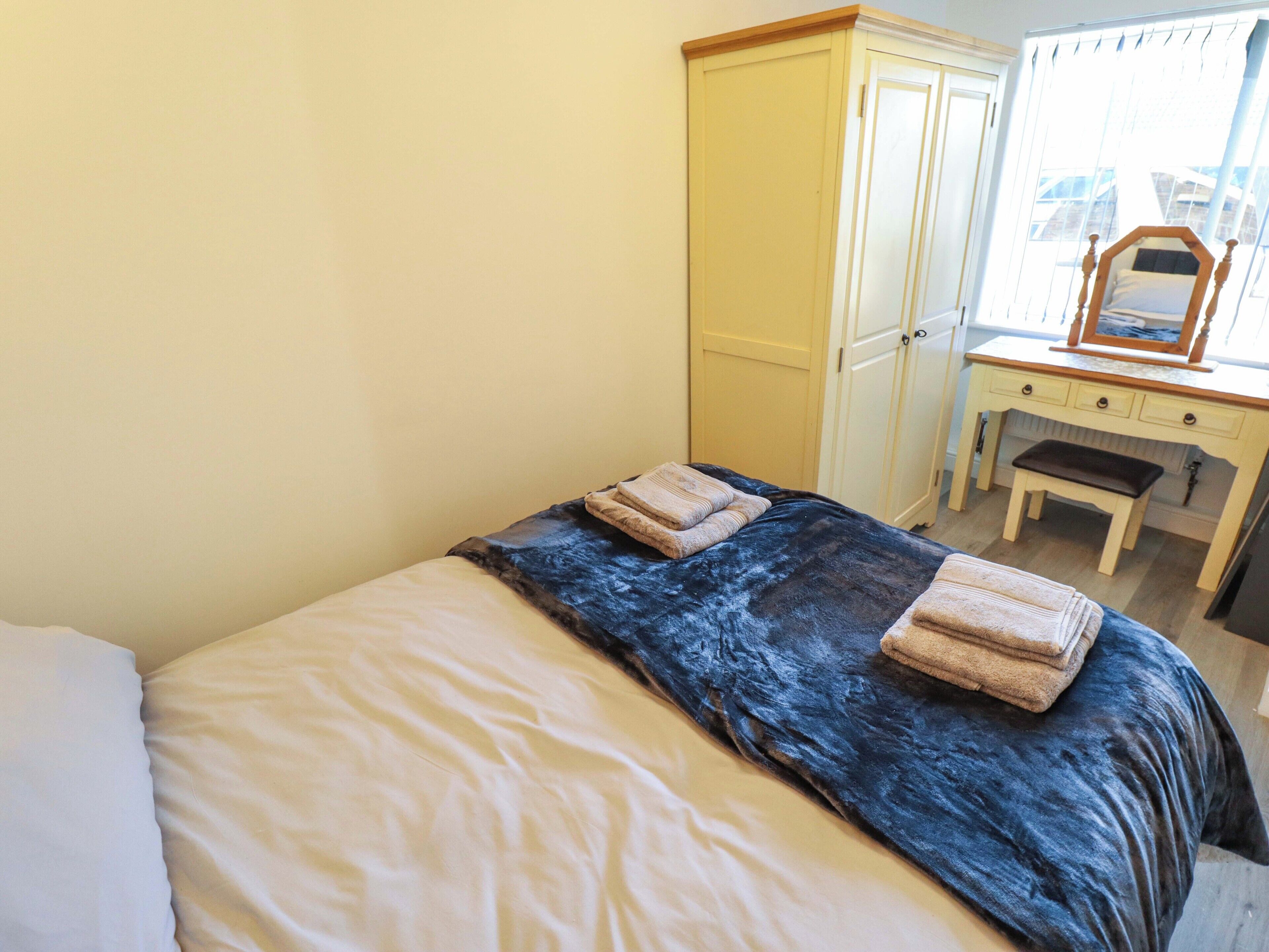 Een slaapkamer met een bed, een kledingkast, een bureau met spiegel en een bankje.