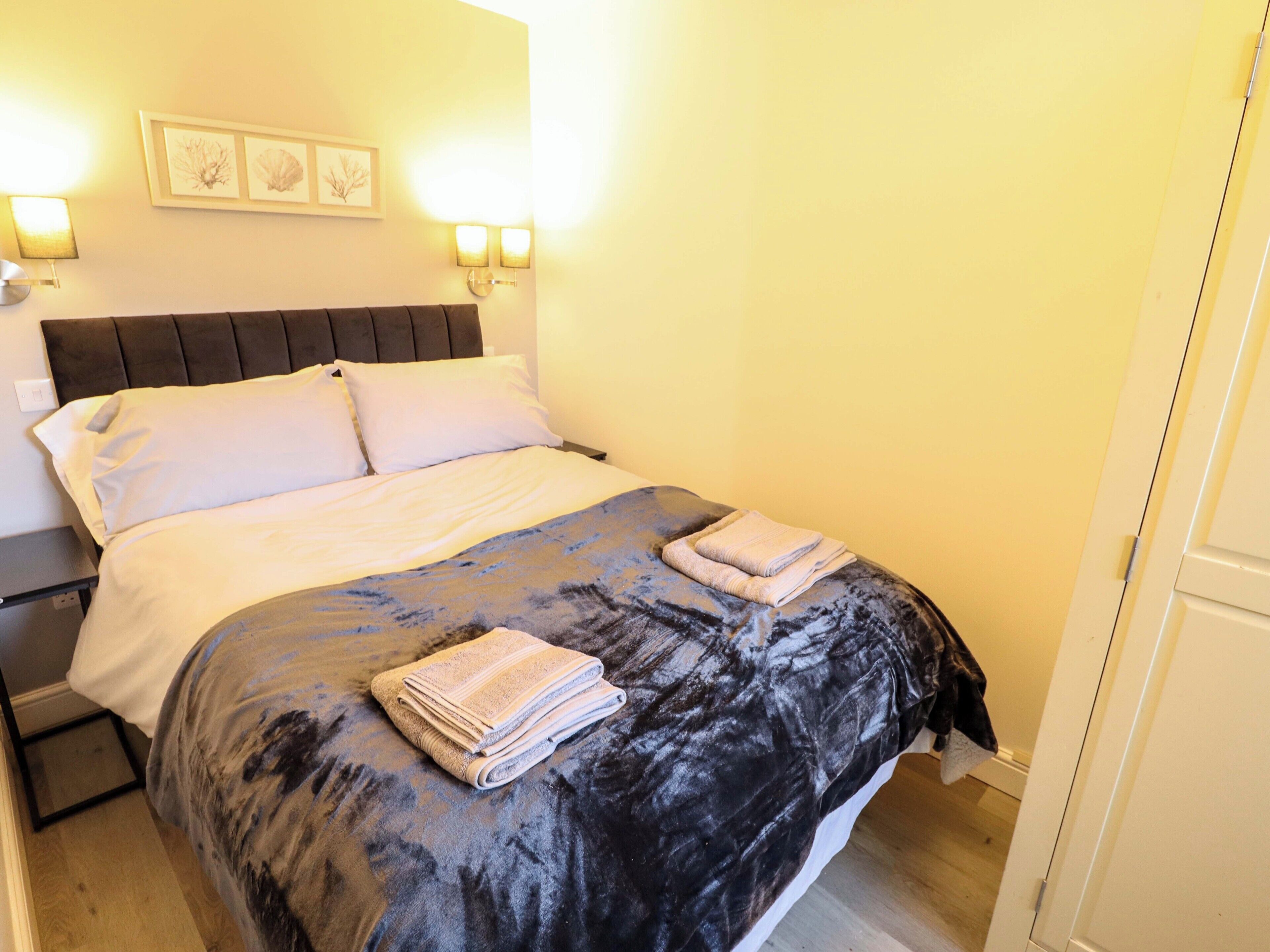 A neatly made bed with a dark patterned bedspread and two folded towels on the foot of the bed.
