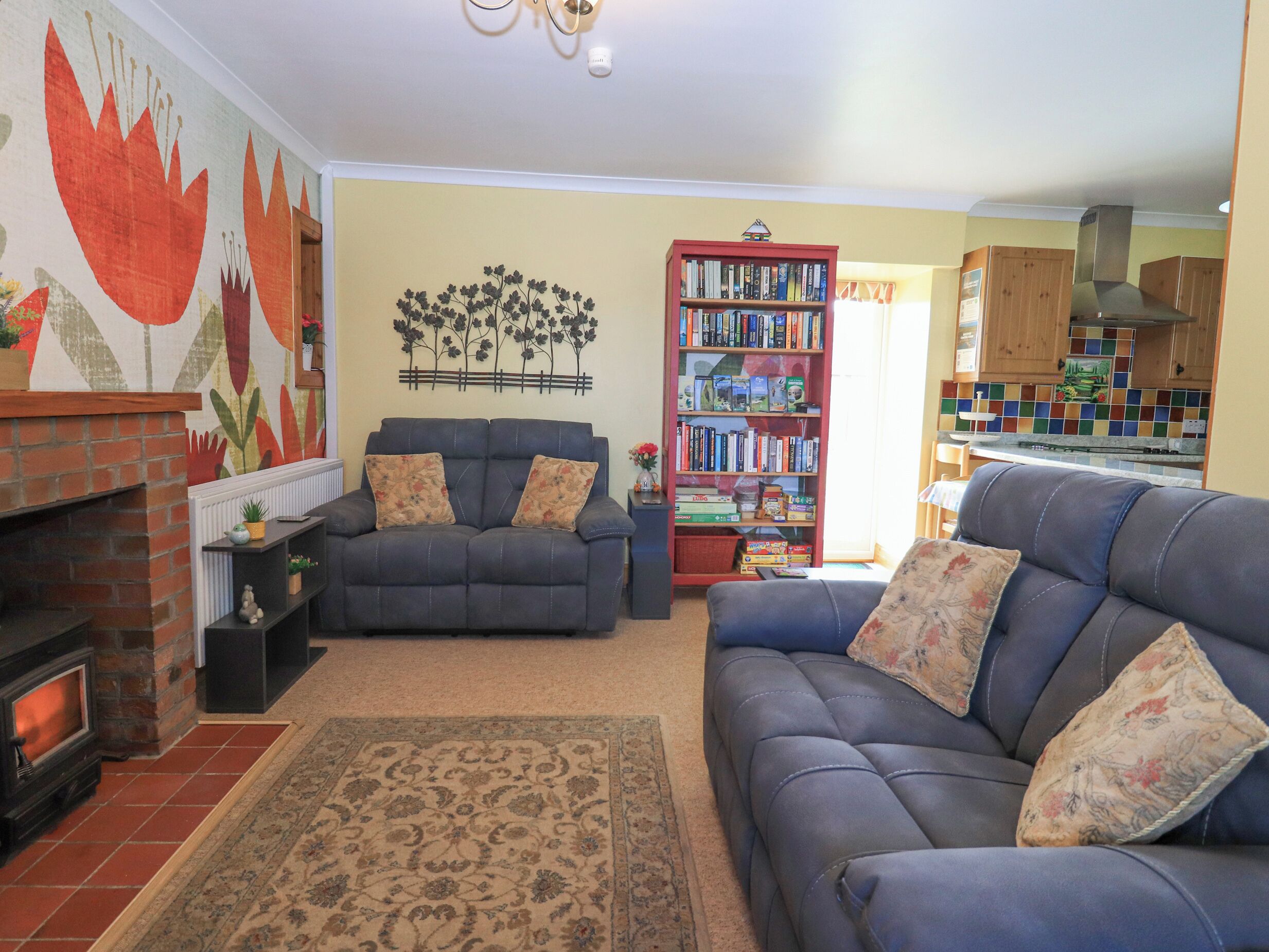 A living room with a fireplace, a sofa, a bookshelf, and a dining area with a tiled backsplash.