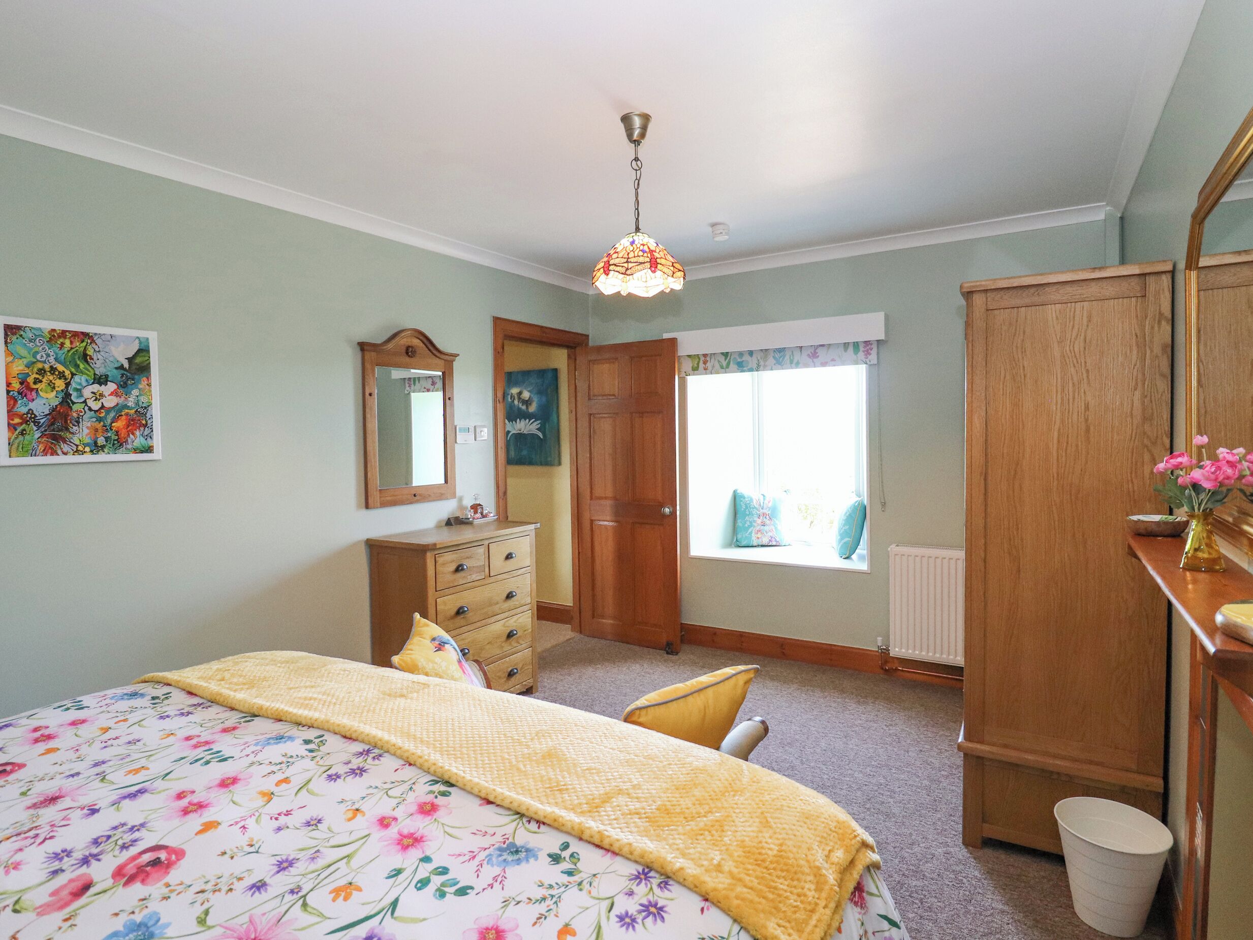 A bedroom with a bed, dresser, mirror, and window.