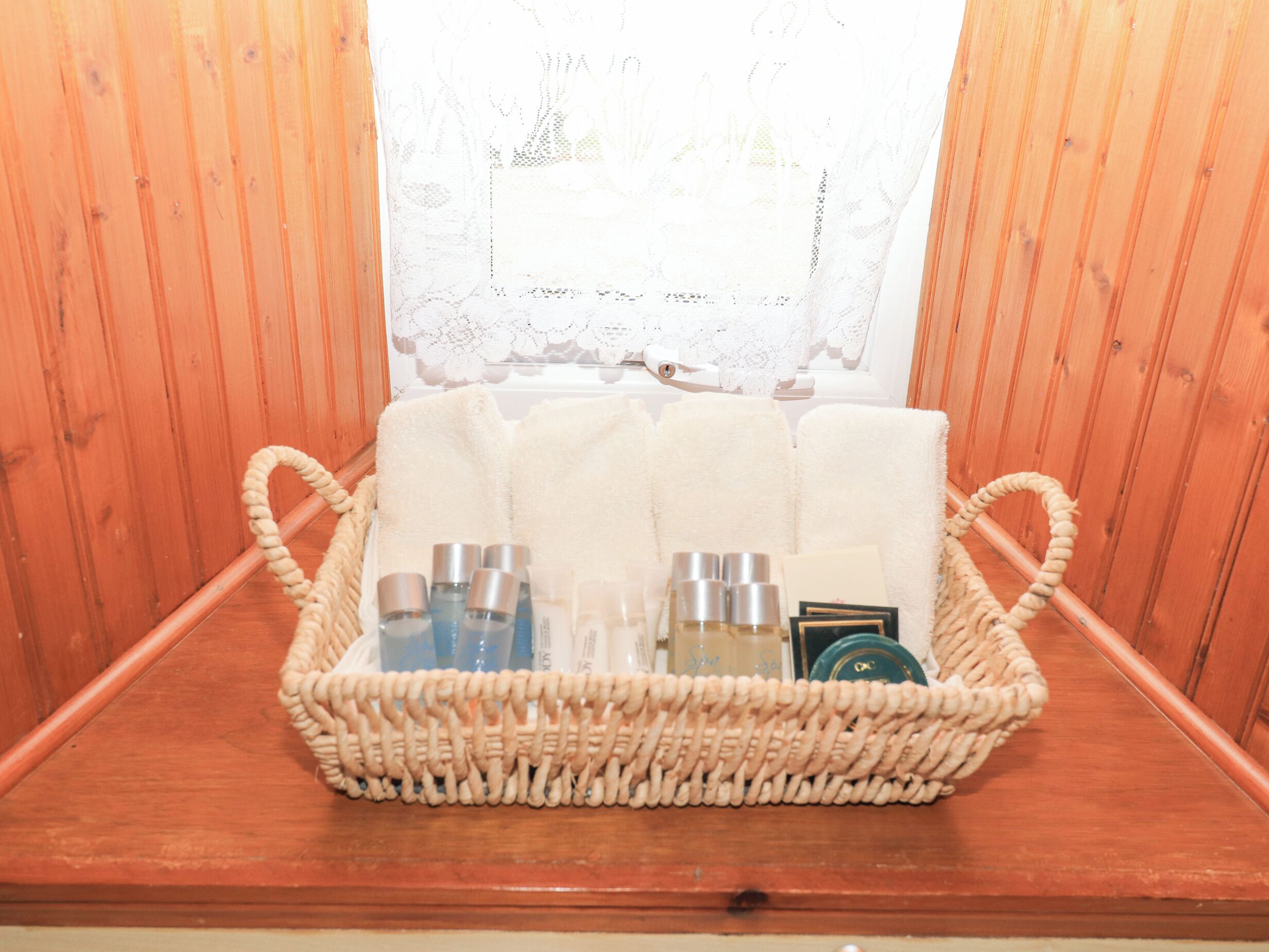 A wooden cabin interior with a woven basket containing toiletries and towels on a wooden bench.