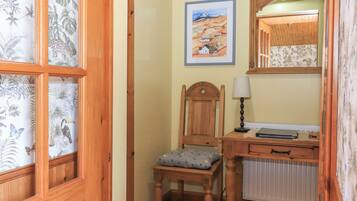 A wooden chair with a cushion, a desk with a lamp, a radiator, and a framed painting on the wall.