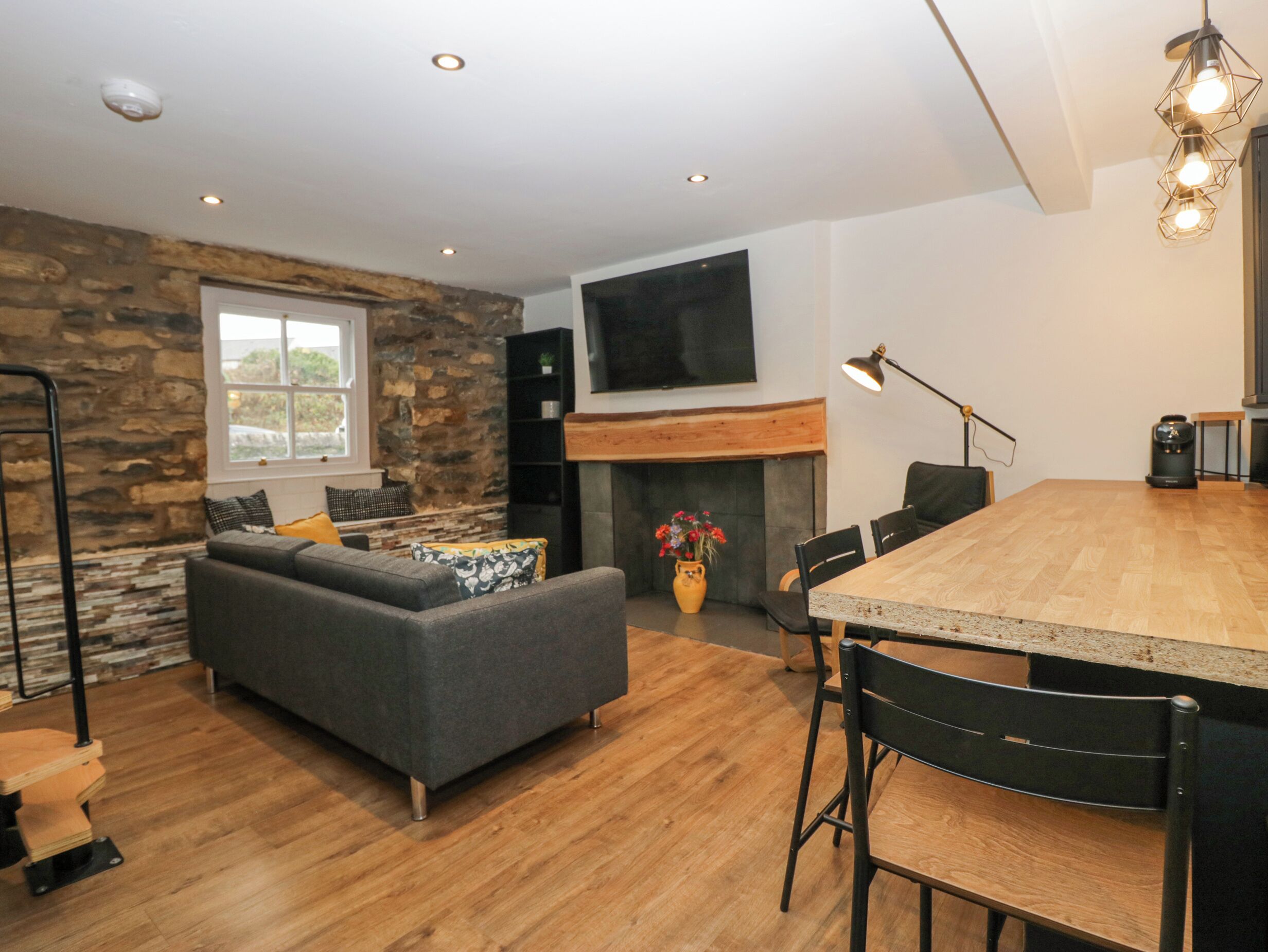 A modern living room with a stone wall, a grey sofa, a wooden dining table, and a fireplace.