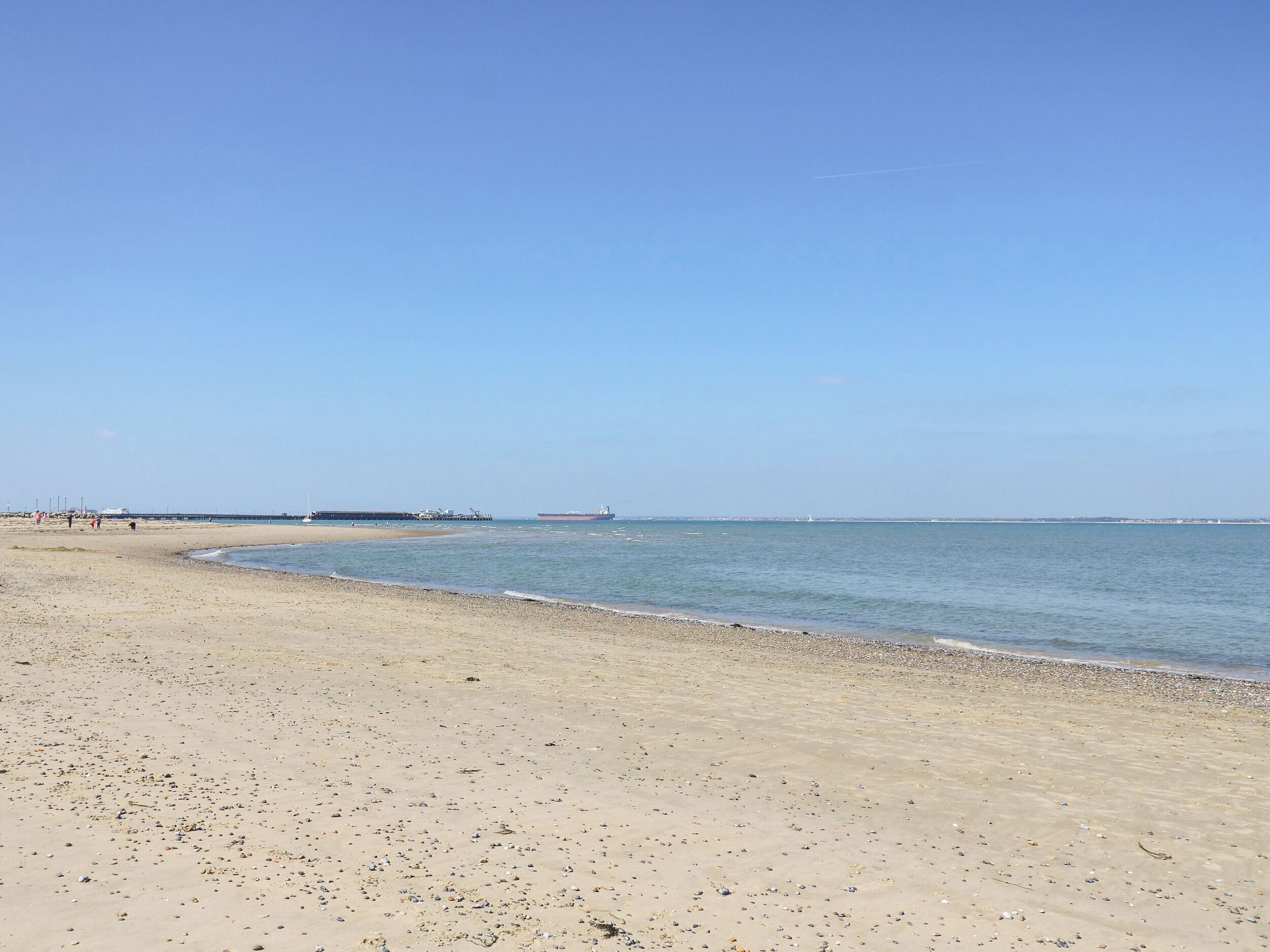 A beach with a pier extending into the water, a large ship in the distance, and a clear sky. - 5A Castle Street (Ryde)