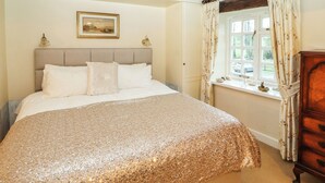 A bedroom with a large bed, a headboard, a window with curtains, a dresser, and a framed picture on the wall. - Stang Farm (Kendal)
