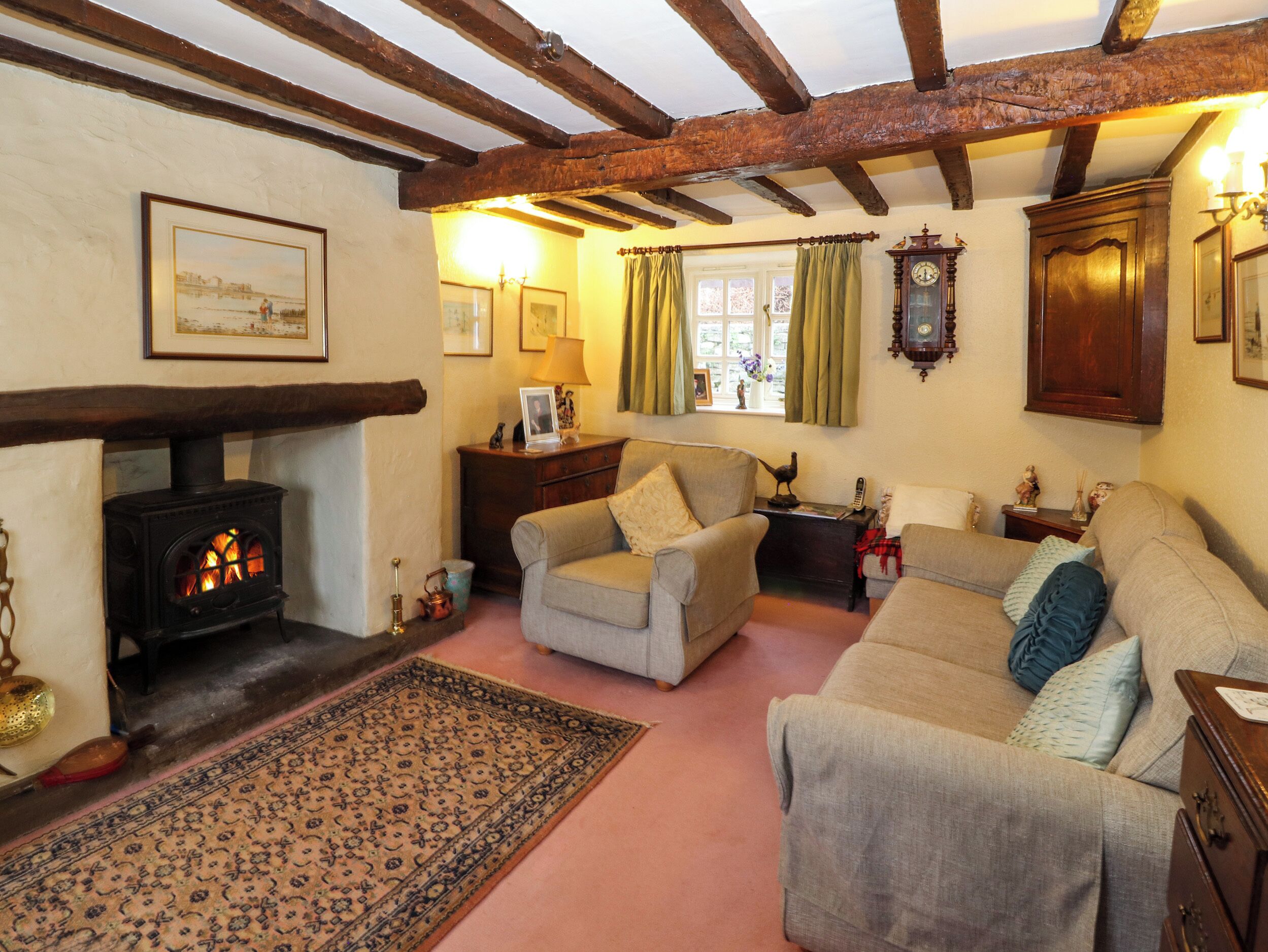A cozy living room with a fireplace, two sofas, a rug, and wooden beams on the ceiling.