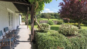 A covered outdoor seating area with stone walls and a pathway leading to a building with white walls and barred windows. - Stang Farm (Kendal)